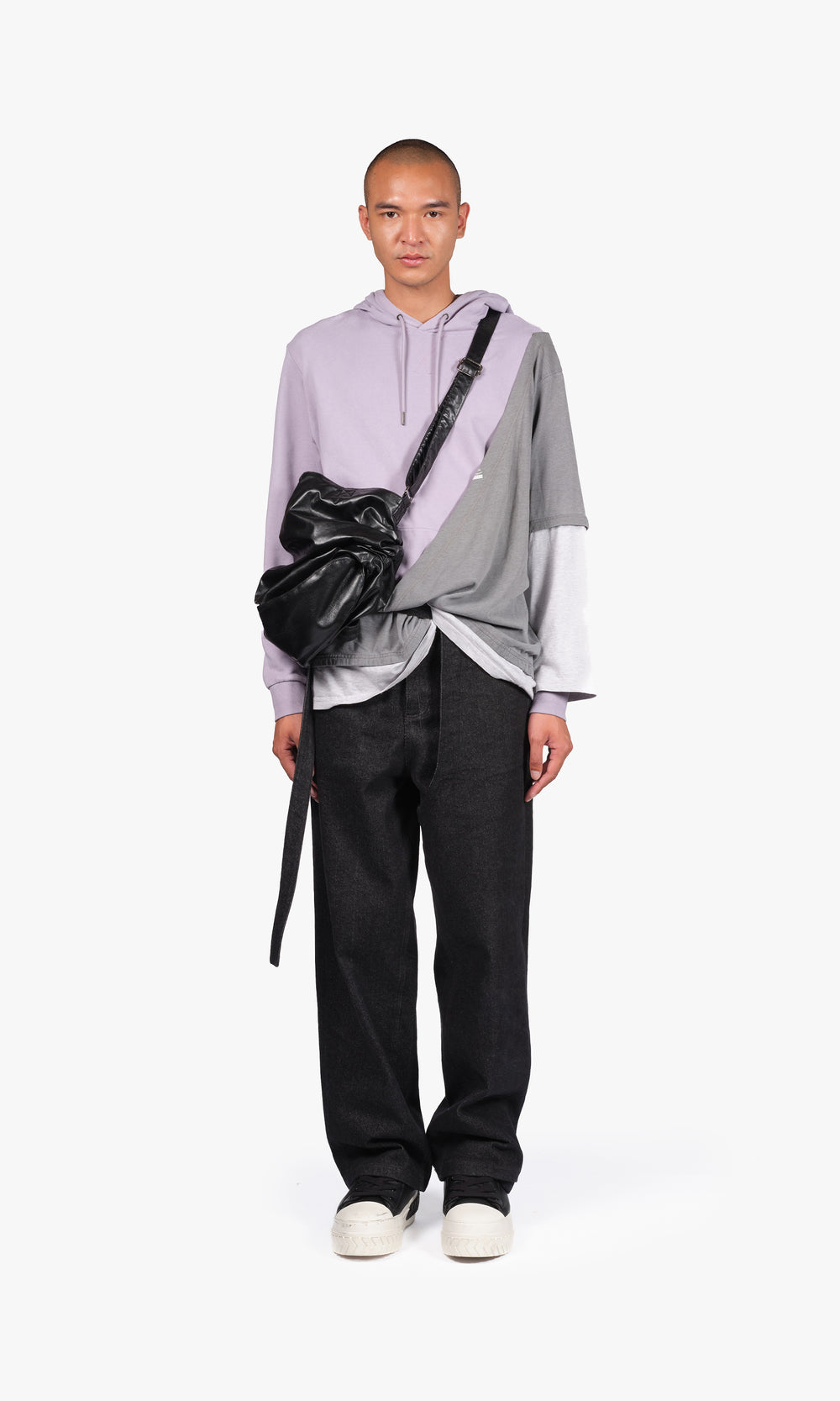 SIEGENTHALER | Front view of the V2 bag in smooth black faux leather, worn crossbody to reveal its fluid silhouette and elongated side strap.