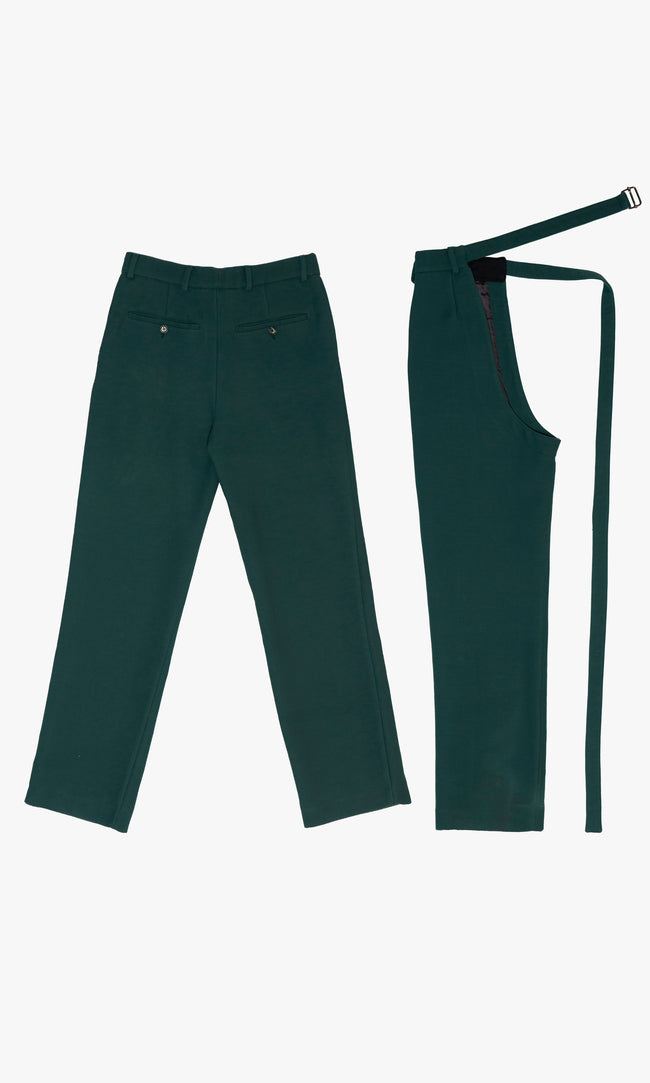 SIEGENTHALER | Back detail view of the modular pants with detachable chaps in forest green wool. Features include buttoned welt pockets, rear darts for structure, and an open-side chap design with an elongated strap, reinforcing the modular and tailored aesthetic of the silhouette.