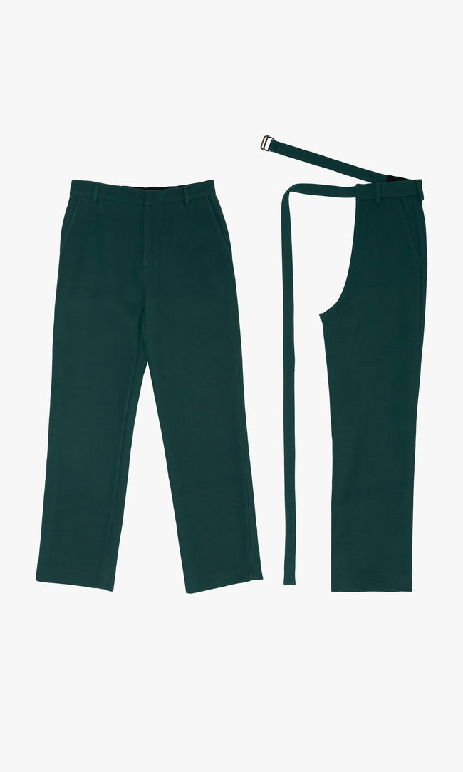 SIEGENTHALER | Front view of the modular tailored pants with detachable chaps in forest green wool. The straight-leg trousers are styled with matching open-side chaps featuring an elongated belt strap and metal buckle, emphasizing versatility and sculptural layering.