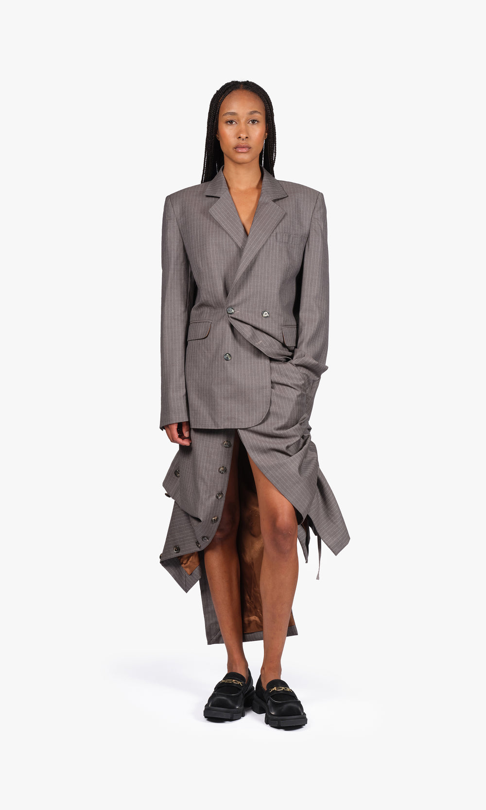 SIEGENTHALER | Front view of the V1 skirt in grey pinstripe wool, styled with matching blazer, featuring layered button closures, asymmetric draping, and exposed copper lining.