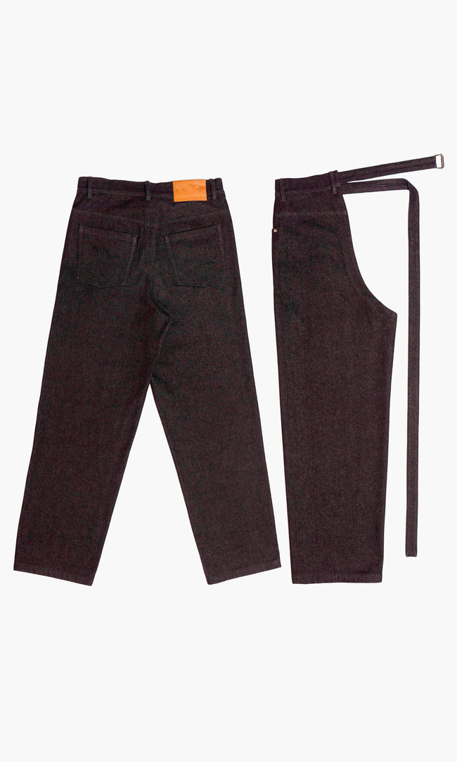SIEGENTHALER | Back view of the modular black denim trouser and chaps. The trousers include rear patch pockets and a leather brand label on the waistband. The chap component mirrors the back seamline and topstitching of the pant, maintaining symmetry when layered.