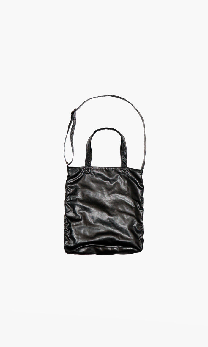 SIEGENTHALER | Front view of the V2 bag in smooth black faux leather, worn crossbody to reveal its fluid silhouette and elongated side strap.