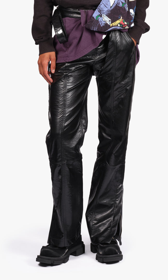 SIEGENTHALER | Front view of the black faux leather pants with chaps, crafted with paneled construction and articulated seams. The layered structure subtly contrasts textures, while the concealed zippers at the hem provide styling adaptability. An embedded belt loop system anchors the detachable chaps, reinforcing the modular silhouette.