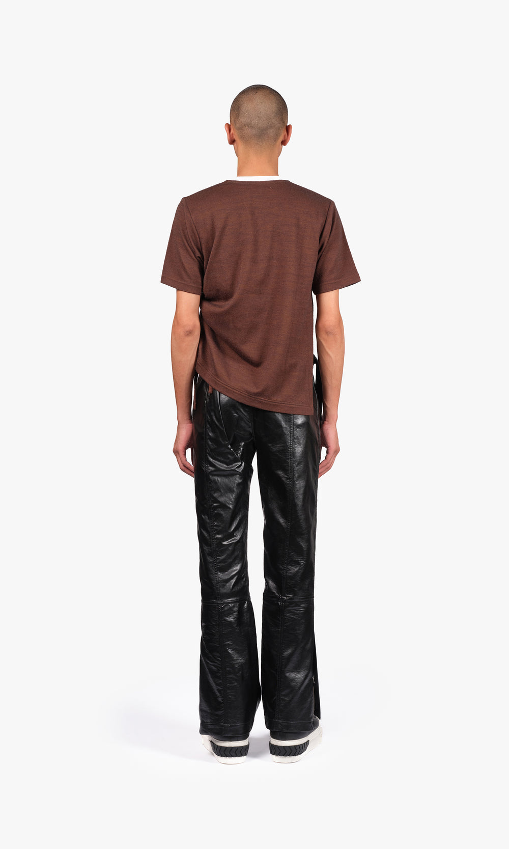 SIEGENTHALER | Back view of the modular pants in black faux leather, revealing the elongated flare cut and clean topstitching, with a slightly twisted leg line enhancing movement.