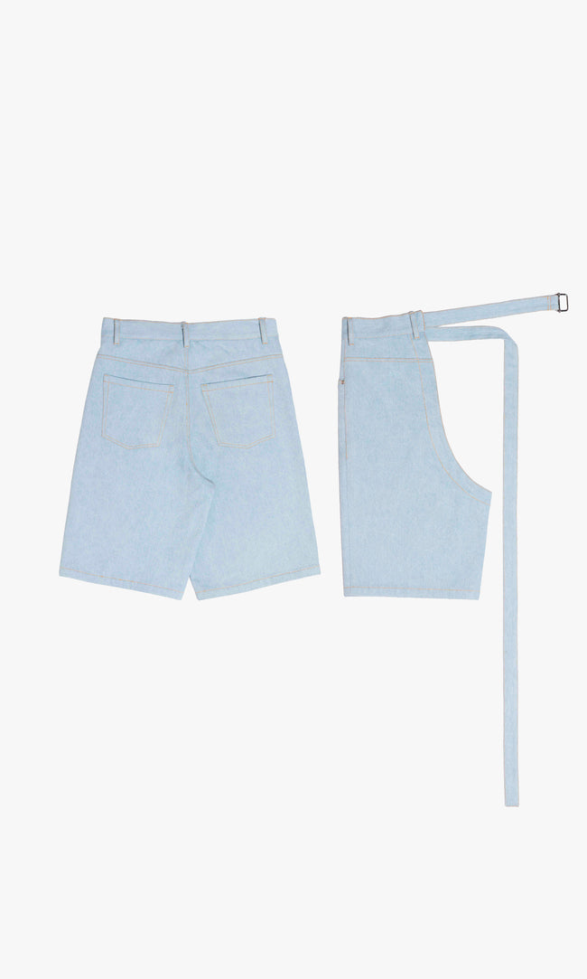 SIEGENTHALER | Rear view of modular light blue denim shorts with functional back pockets and curved panel lines. Comes with detachable wrap piece for convertible styling and utilitarian contrast.